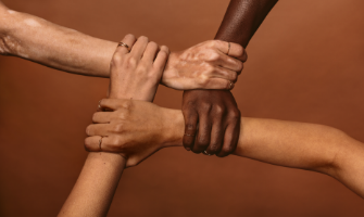Four arms and hands shown interlinked. Four different skin tones